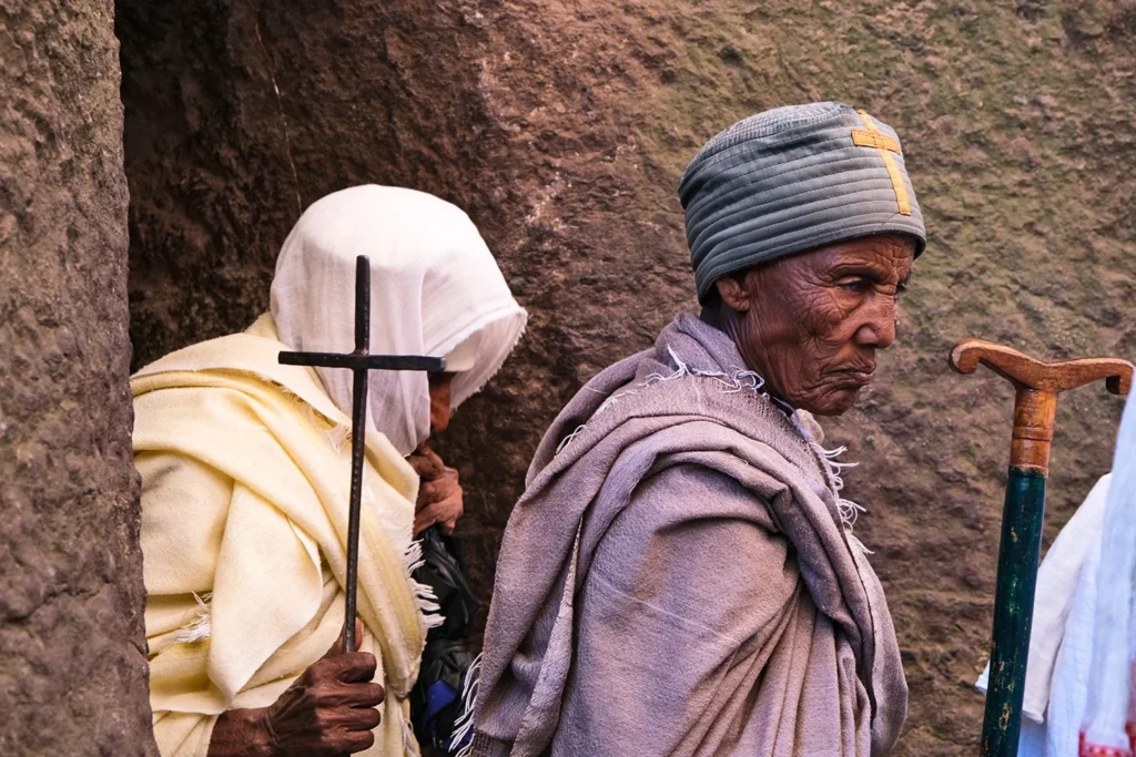 Ηλικιωμένοι πιστοί στη Lalibela, γυναίκα με λευκό μαντήλι κρατά σταυρό και άνδρας με μπαστούνι στέκεται δίπλα της