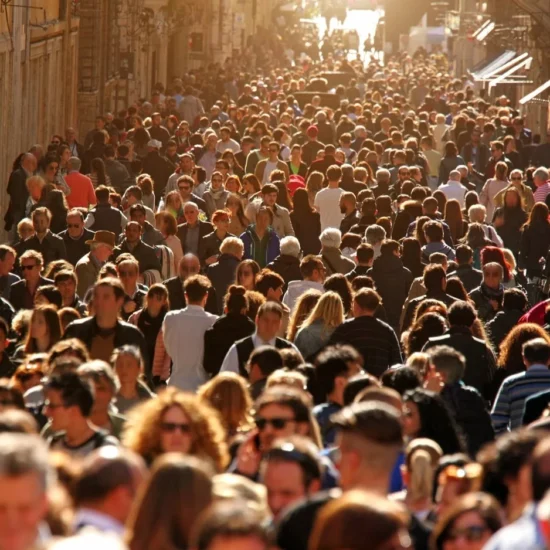 Πλήθος επισκεπτών γεμίζει έναν στενό δρόμο ανάμεσα σε παλιά κτίρια και καταστήματα