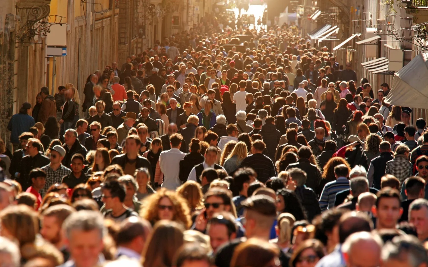 Πλήθος επισκεπτών γεμίζει έναν στενό δρόμο ανάμεσα σε παλιά κτίρια και καταστήματα